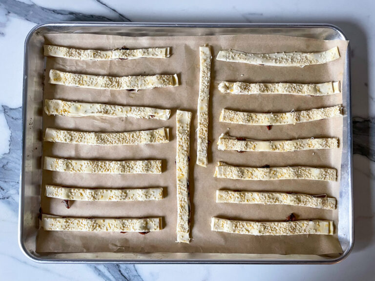 Rows of unbaked anchovy sticks on a parchment lined tray