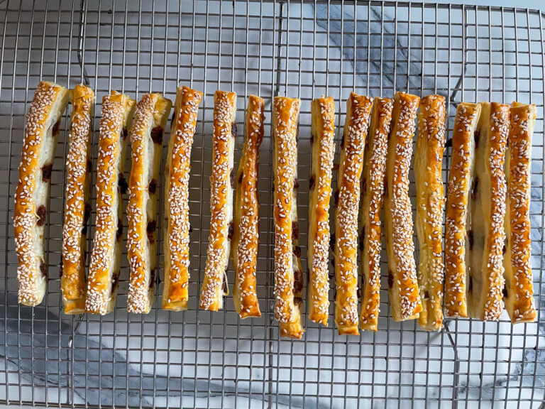 Puff pastry anchovy sticks arranged in a row on a wire cooling rack