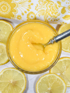 Lemon curd in a dish with lemons and a tea towel