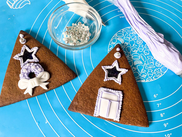 Piping bags of royal icing, bowl of sprinkles, and two triangular gingerbread house pieces
