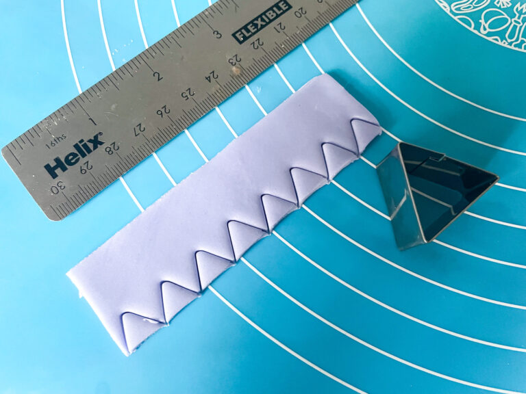 Purple fondant and a triangle cutter on a silicone mat