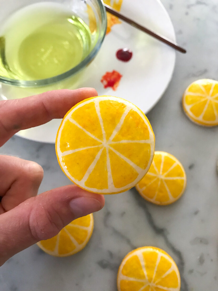 Hand holding a painted lemon macaron shell