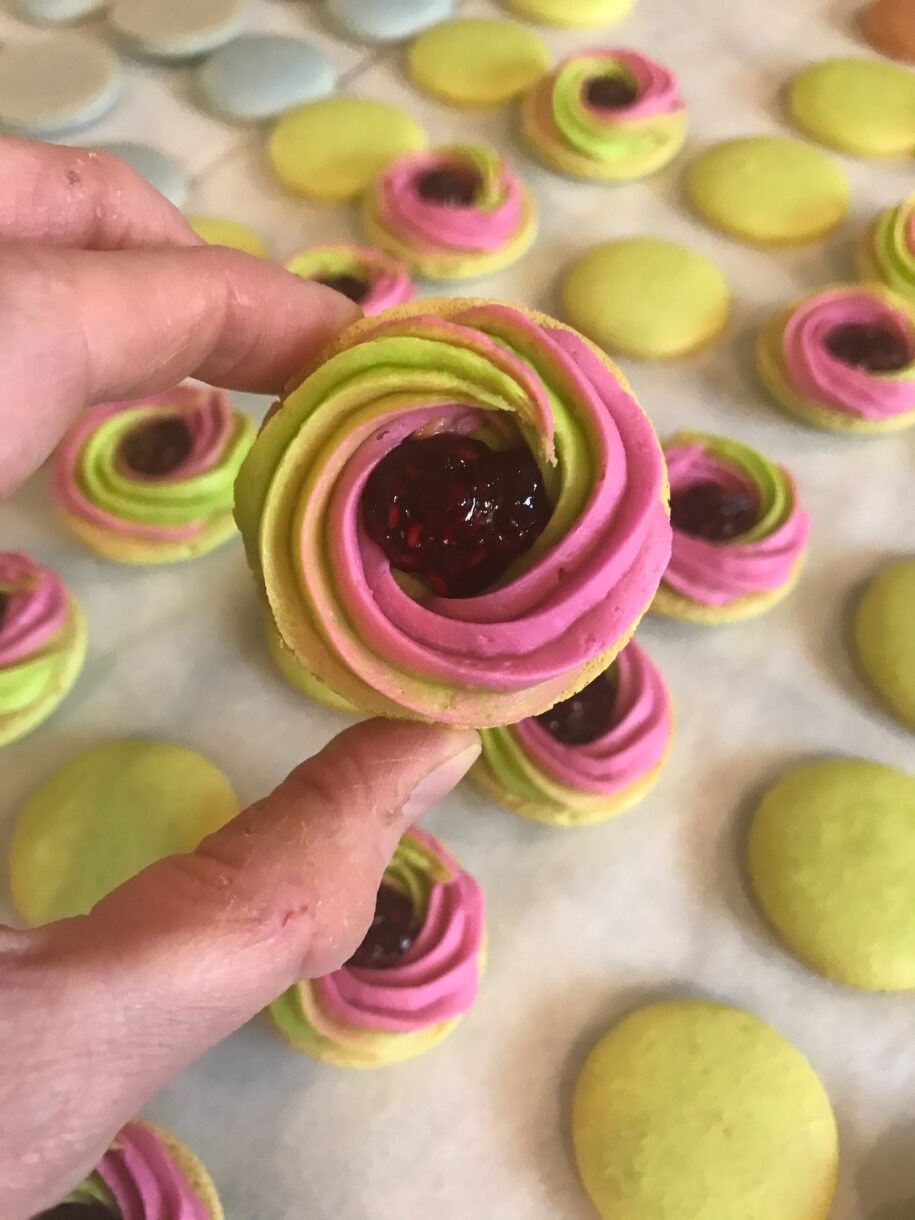 Hand holding a macaron shell with buttercream and jam