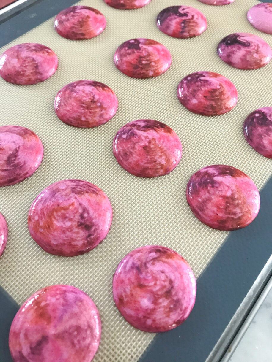 Unbaked pink macaron shells on silicone mat
