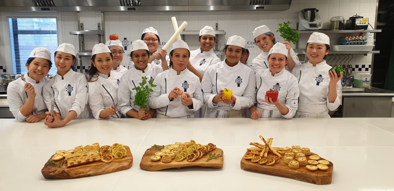 Students in Le Cordon Bleu uniforms in the kitchen with puff pastry appetizer trays on countertop