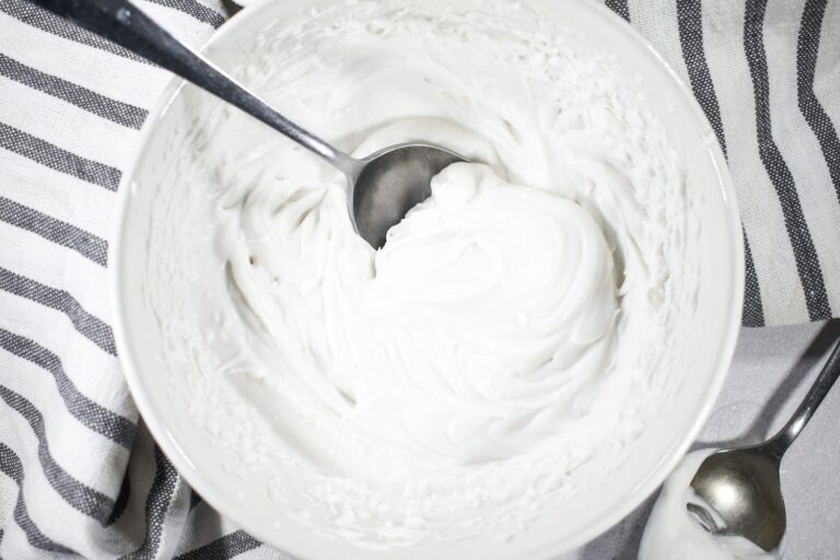 A white bowl of coconut whipped cream, striped tea towel, and a spoon