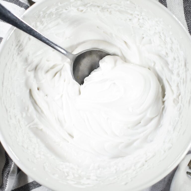 A white bowl of coconut whipped cream, striped tea towel, and a spoon