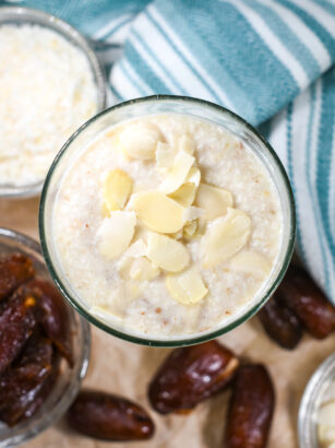 An almond milk smoothie in a glass, with a bowl of coconut, dates, and a tea towel