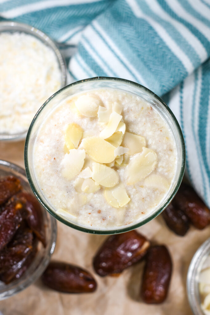 An almond milk smoothie in a glass, with a bowl of coconut, dates, and a tea towel
