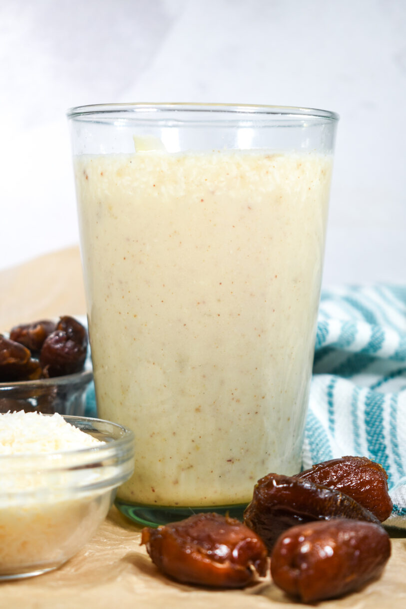 Date smoothie in a glass, with a bowl of coconut, dates, and a tea towel