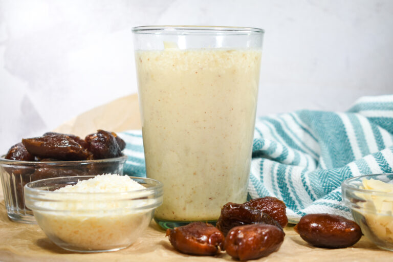 Banana and date smoothie in a glass, with a bowl of coconut, dates, and a tea towel