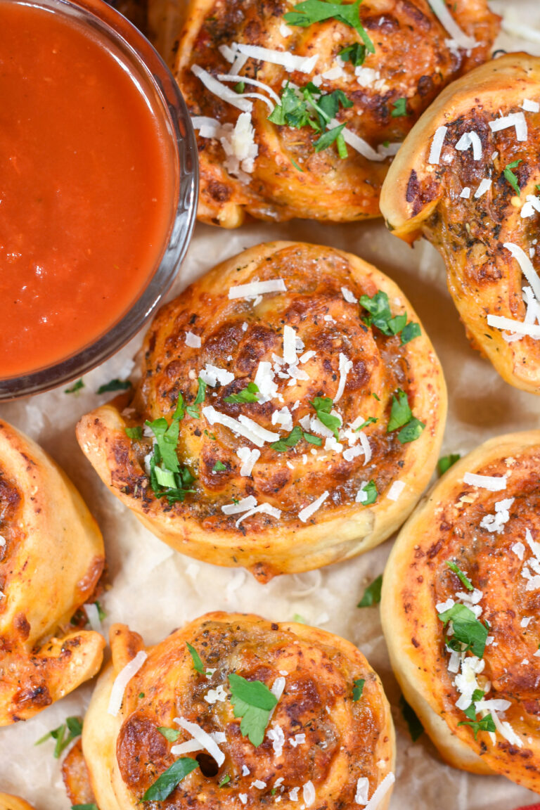 Cheese pizza rolls and a dish of pizza sauce on a sheet of parchment