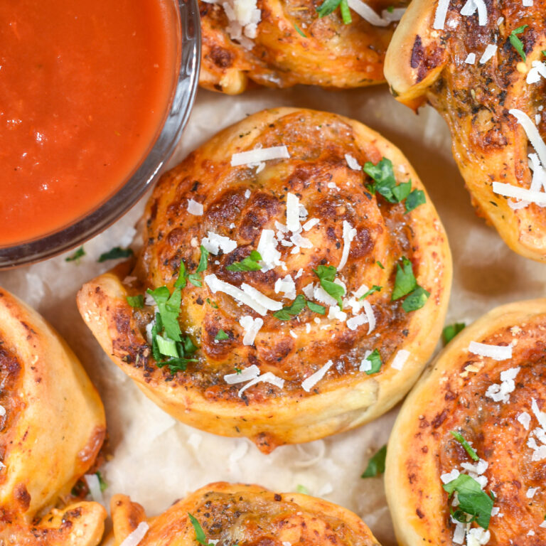 Cheese pizza rolls and a dish of pizza sauce on a sheet of parchment