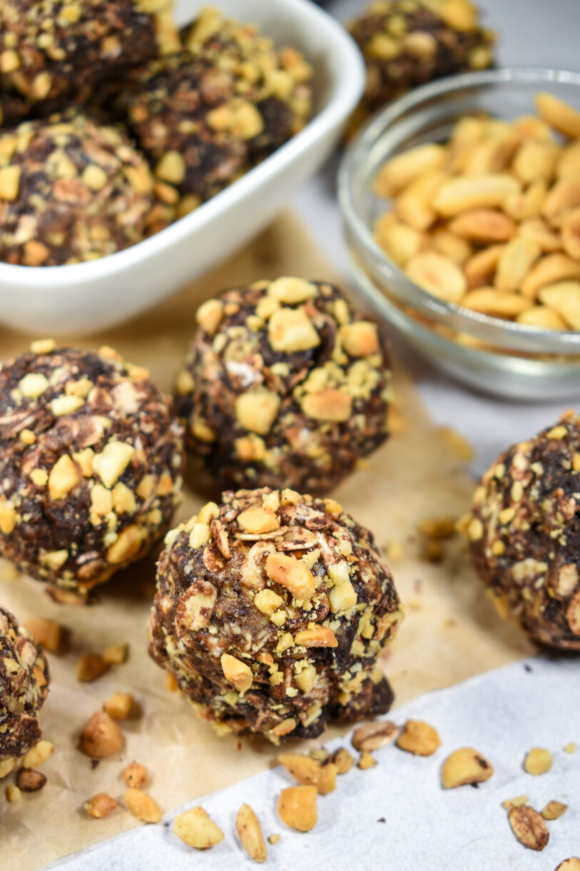 Chocolate oatmeal bites rolled in peanuts, on a sheet of baking parchment