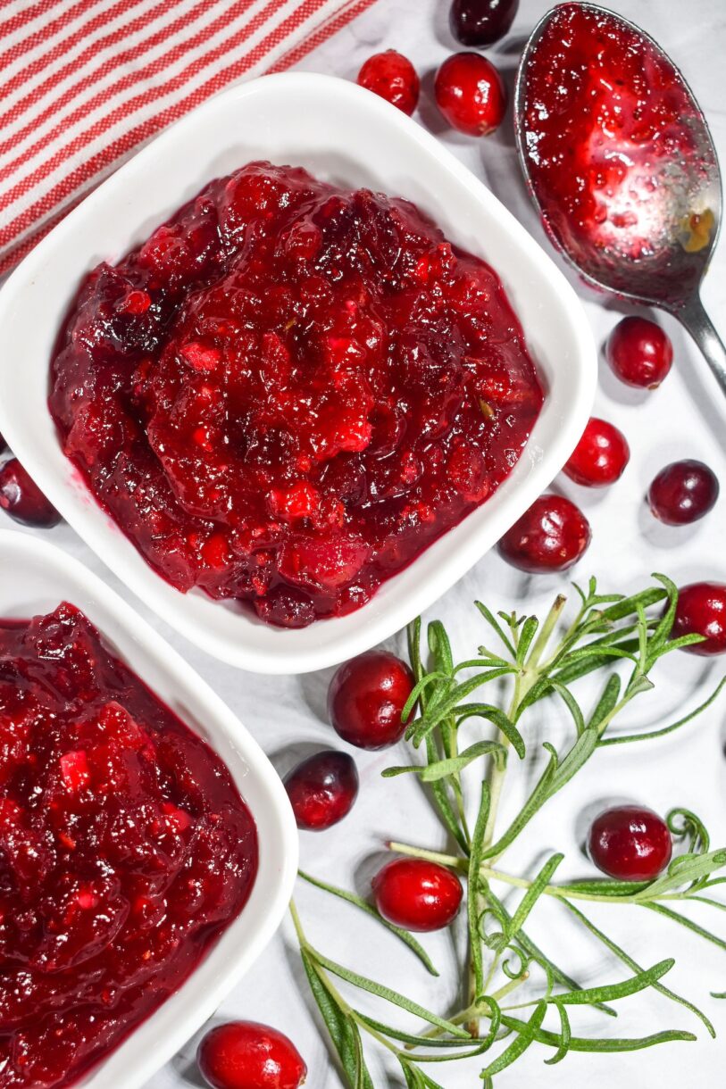 A sprig of rosemary, red cranberry and orange compote, and fresh cranberries