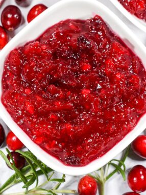 Cranberry compote in a bowl surrounded by cranberries and a red striped tea towel