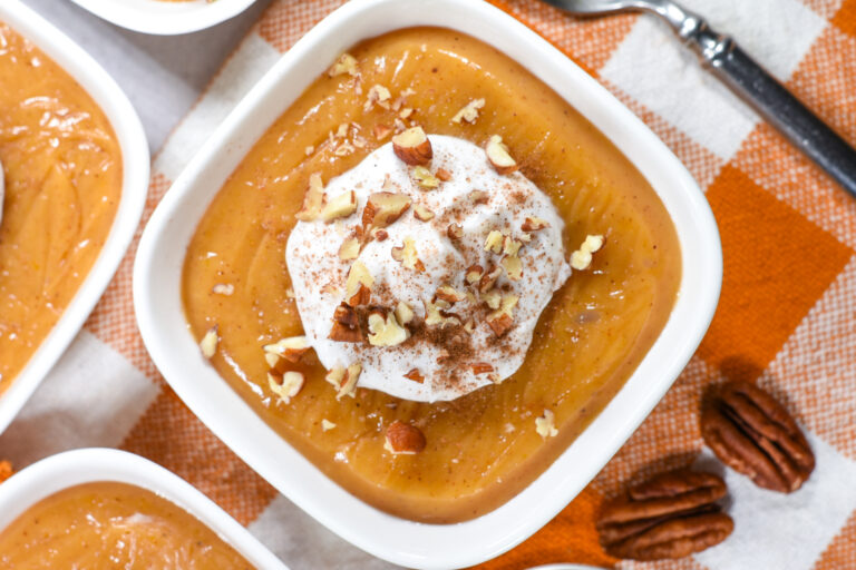 Butternut custard topped with coconut whipped cream, on an orange checkered towel with a spoon