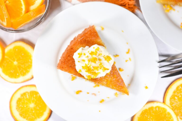 Flourless almond cake slice on a plate, surrounded by oranges