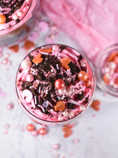 Looking down at a parfait with pink whipped cream, crushed oreos and sprinkles