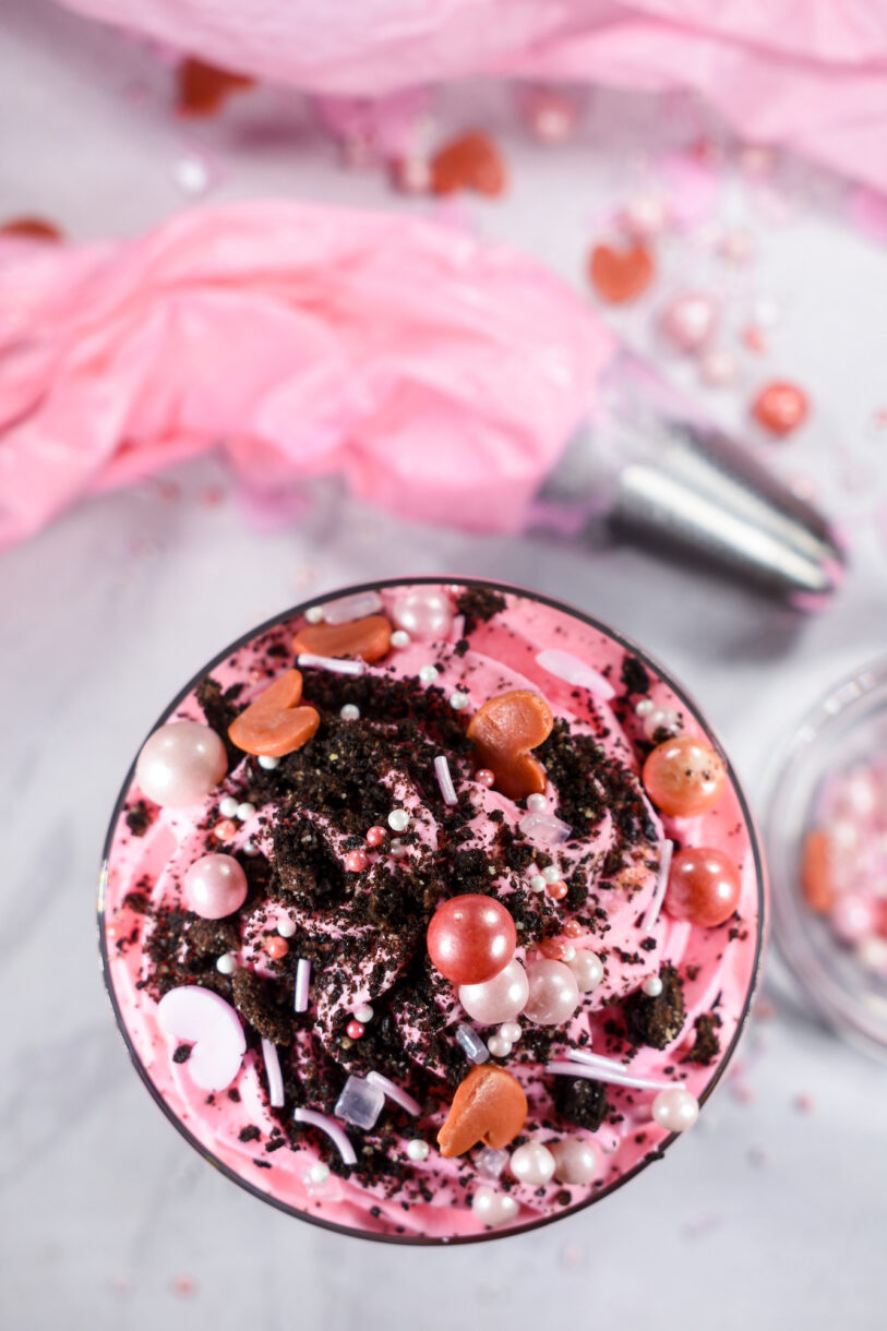 Looking down at a Valentine's Day dessert parfait with pink whipped cream, crushed oreos and sprinkles