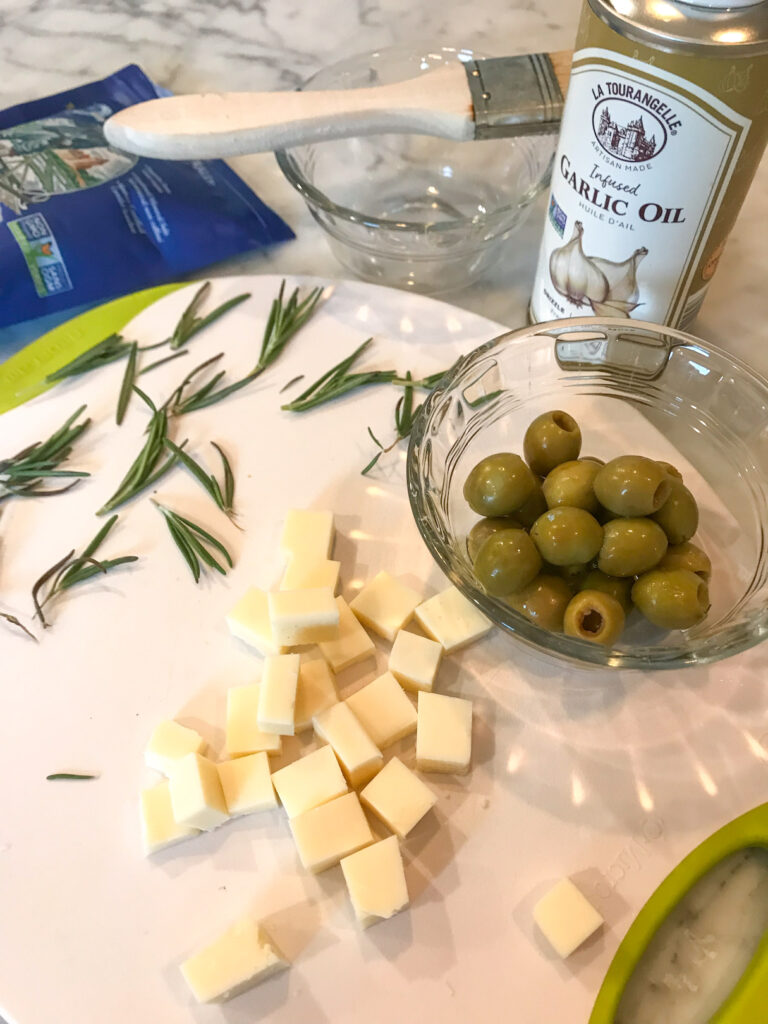 Cheese, salt, olives, and olive oil on a white cutting board