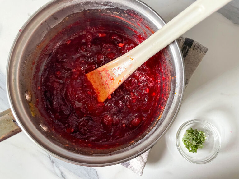 Cranberry compote in pan on marble countertop with a tiny bowl of chopped rosemary