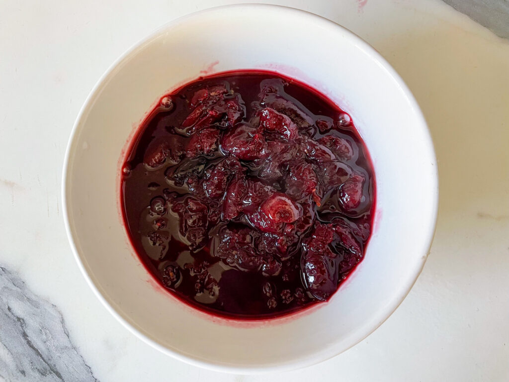 A bowl of cherry compote on a marble countertop