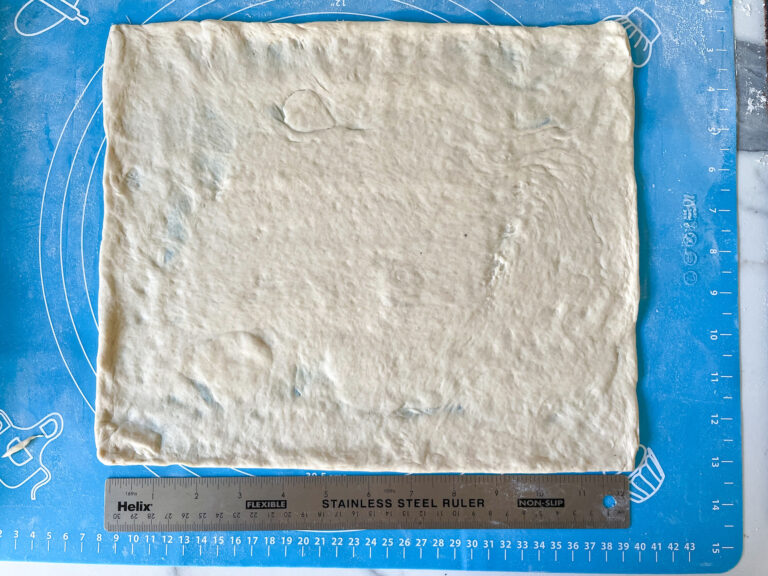 Homemade pizza dough and a ruler on a silicone mat