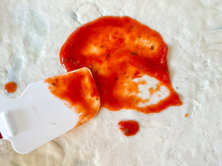 A spatula spreading sauce on pizza dough