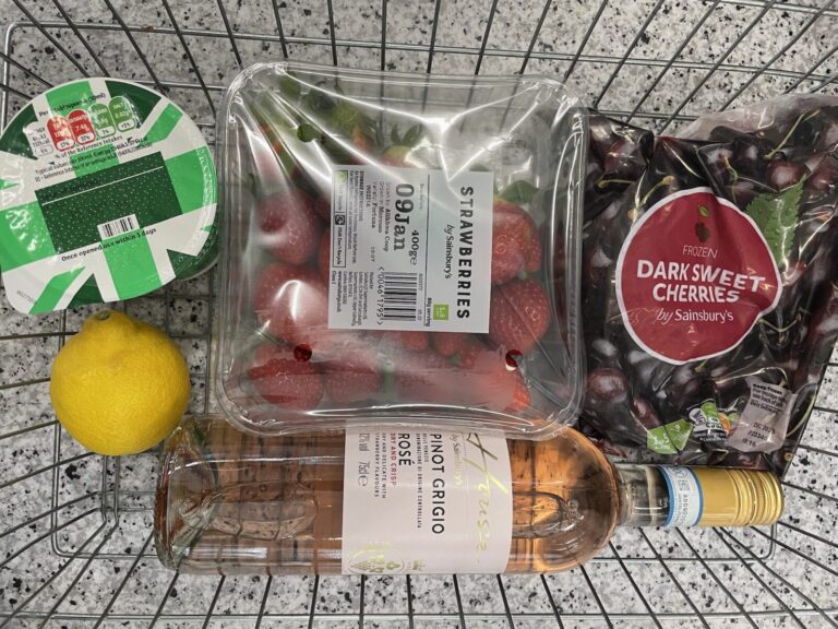 A grocery shopping basket with cherries, rose wine, strawberries, and cream