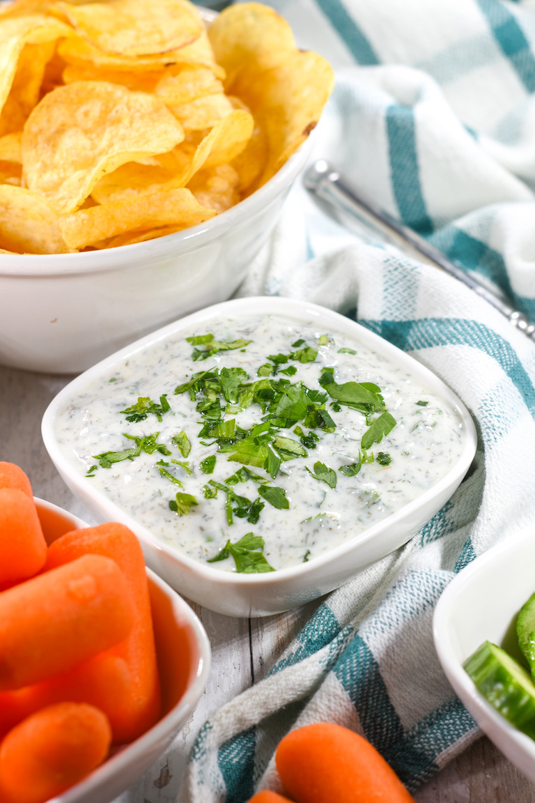 Greek yogurt dip garnished with parsley, next to chips, carrots, and a tea towel