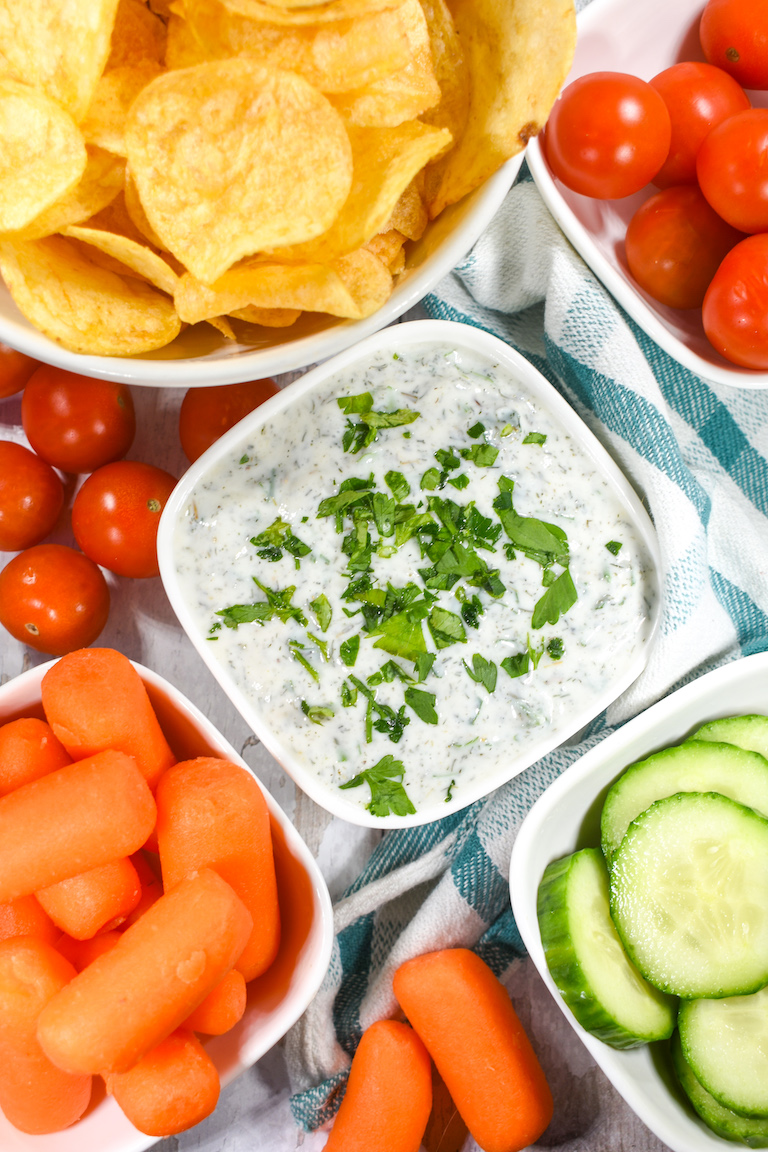 Healthy Greek yogurt dipping sauce in a white bowl, next to bowls of chips and raw vegetables