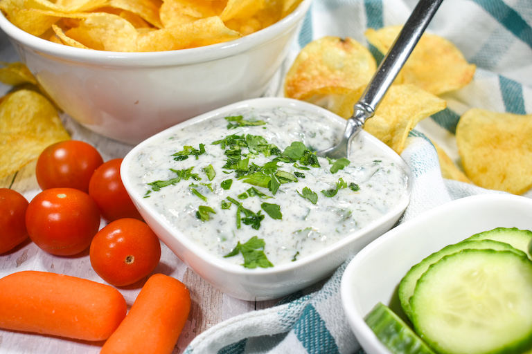 Healthy yogurt dip in a bowl, surrounded by chips and raw vegetables