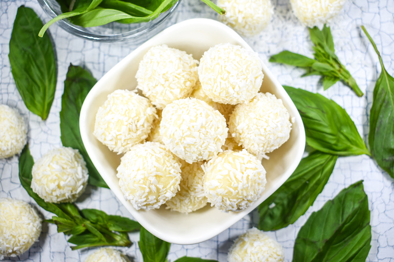 Bowl of coconut cream truffle balls and fresh basil leaves
