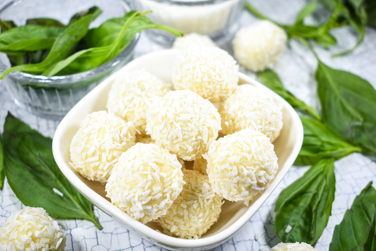 A bowl of coconut milk truffle balls surrounded by basil leaves