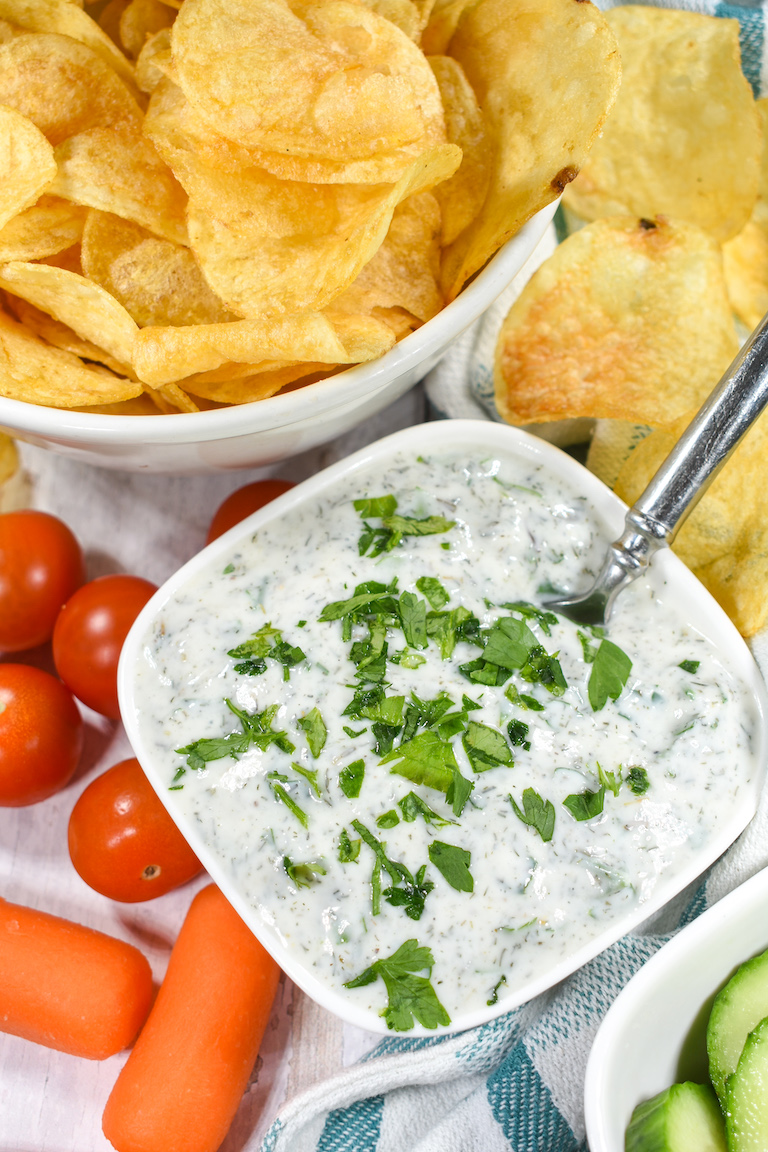 Yogurt dip for veggies, in a bowl with a spoon, alongside chips and raw vegetables