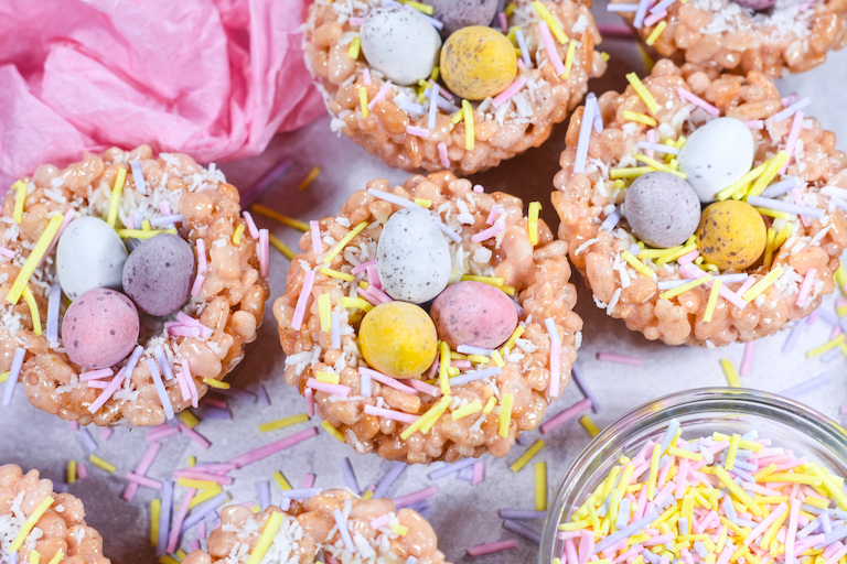 Easter rice krispie bird nest treats on a white surface, with bowl of sprinkles and pink tissue paper
