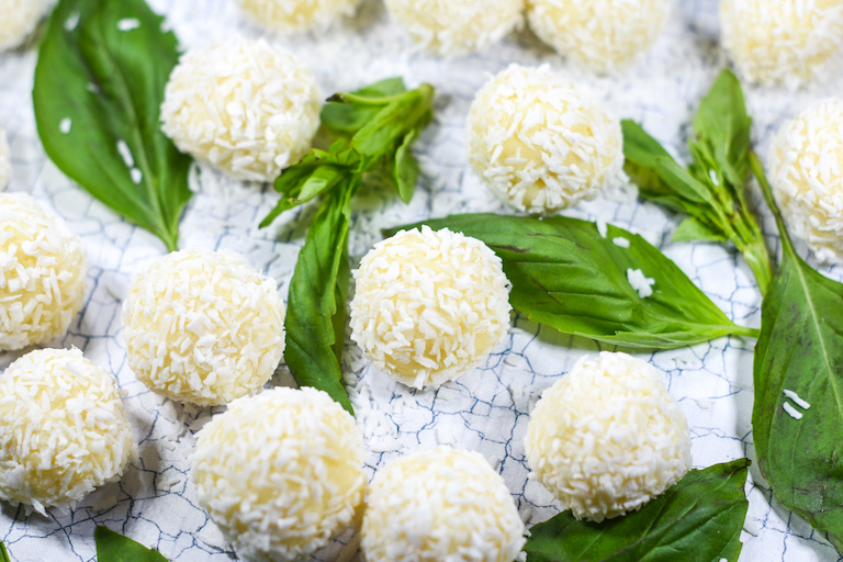 Easy coconut truffles arranged on a white surface with basil leaves