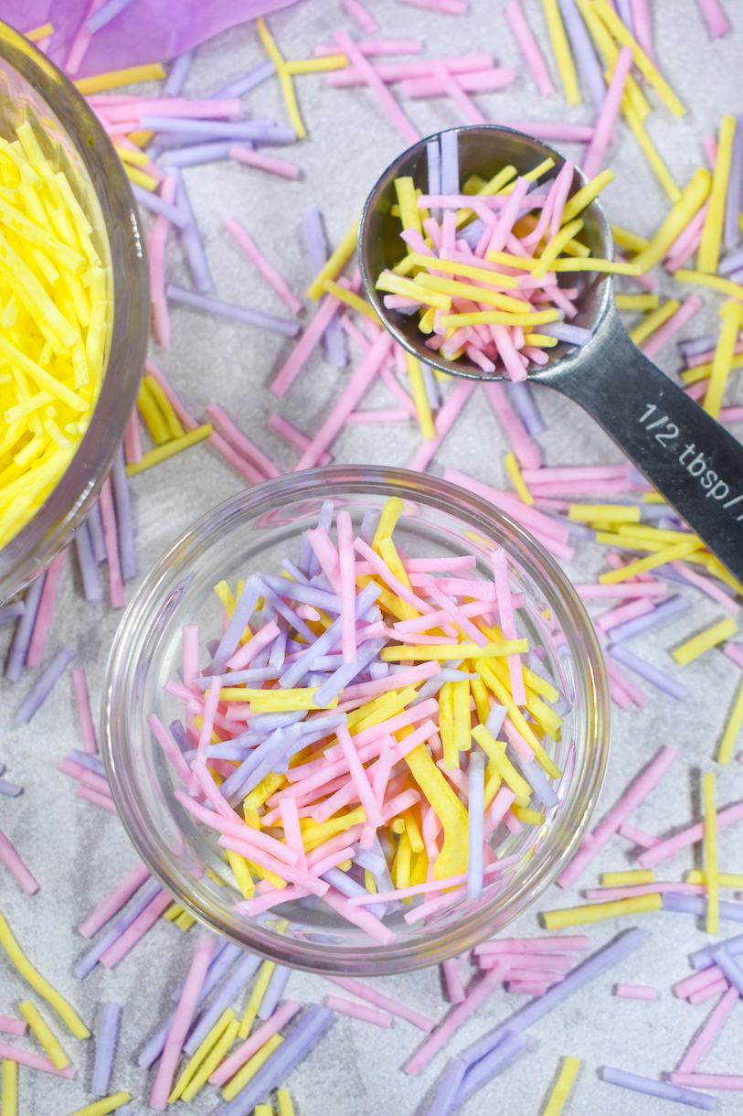 Dish of DIY sprinkles, tablespoon, and sprinkles scattered on countertop