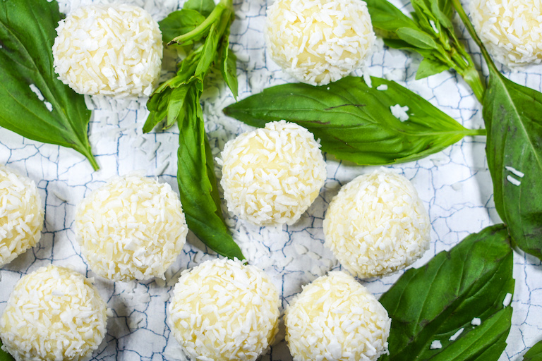 Chocolate coconut truffle balls and basil leaves on a textured white surface