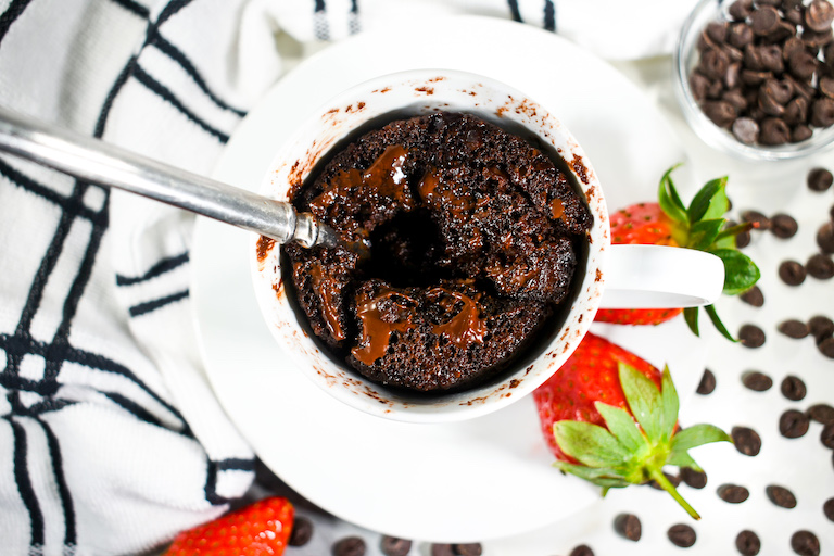 Looking down into a chocolate mug cake, sitting on a plate with strawberries and surrounded by chocolate chips