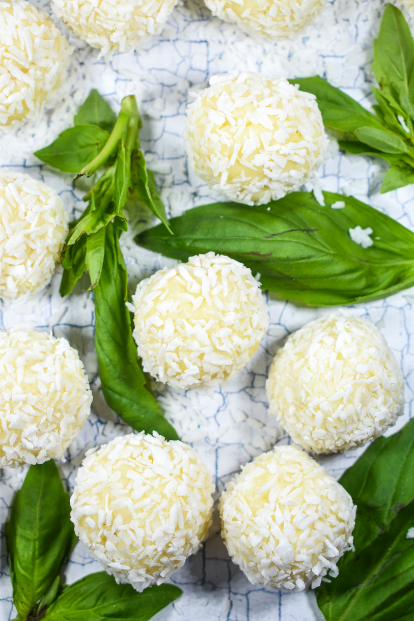 White chocolate truffles, surrounded by fresh basil leaves, on a white surface