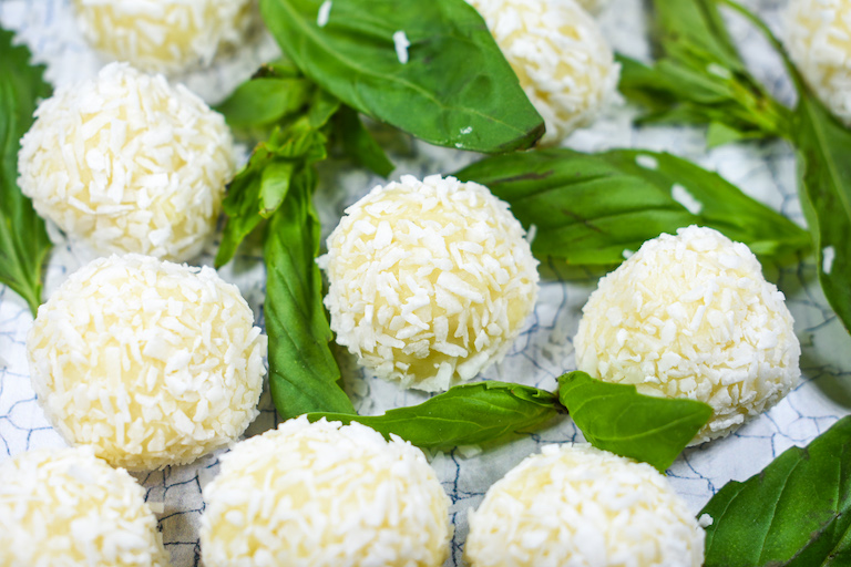 White chocolate truffles rolled in coconut, surrounded by basil leaves