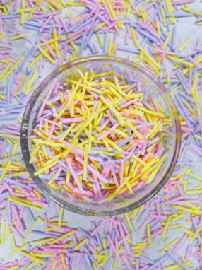 A glass dish of yellow, pink, and purple homemade sprinkles