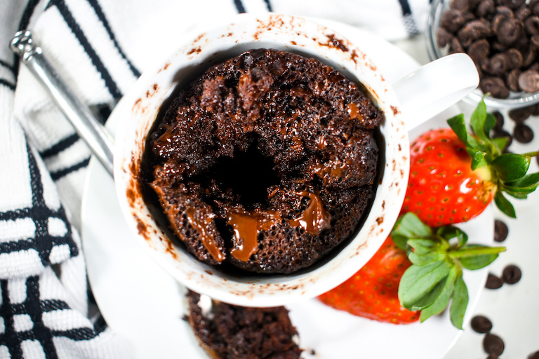 Looking down into a gooey chocolate mug cake, on a plate with strawberries