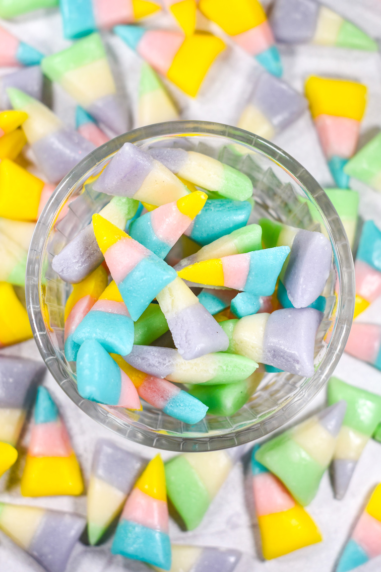 a bowl of pastel colored candy corn on a white surface