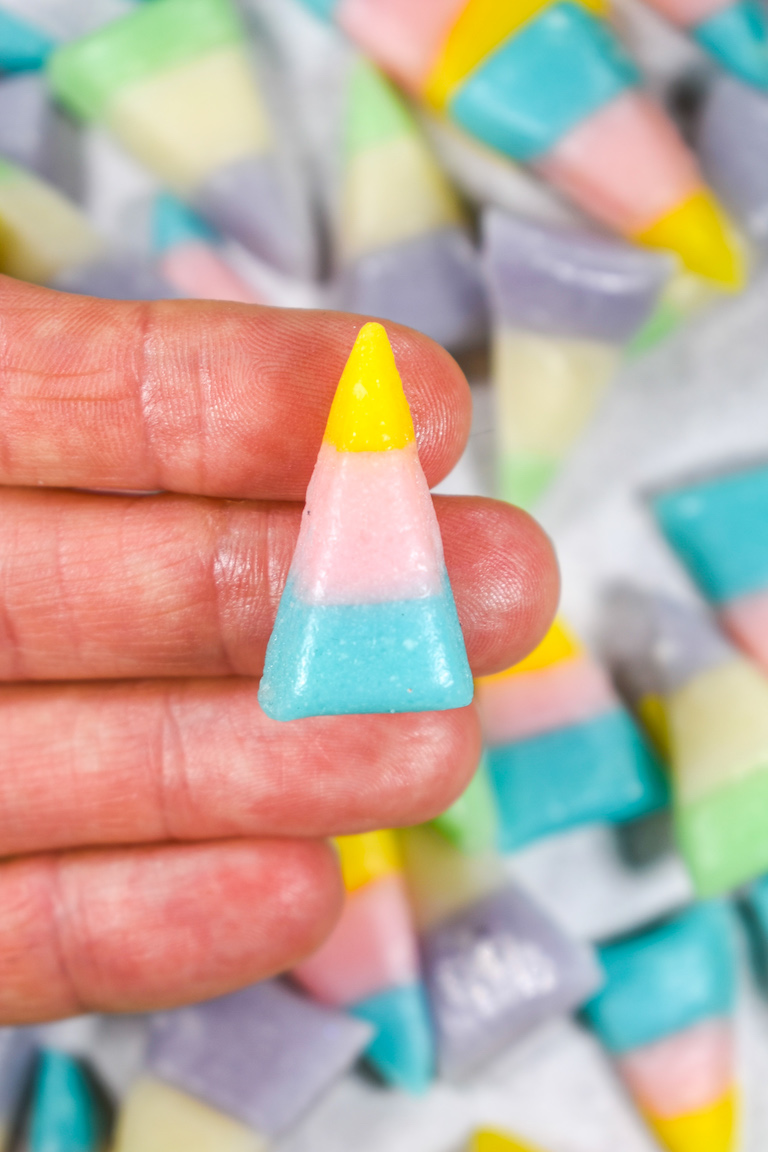 Hand holding a pink, yellow, and blue kernel of Easter candy corn