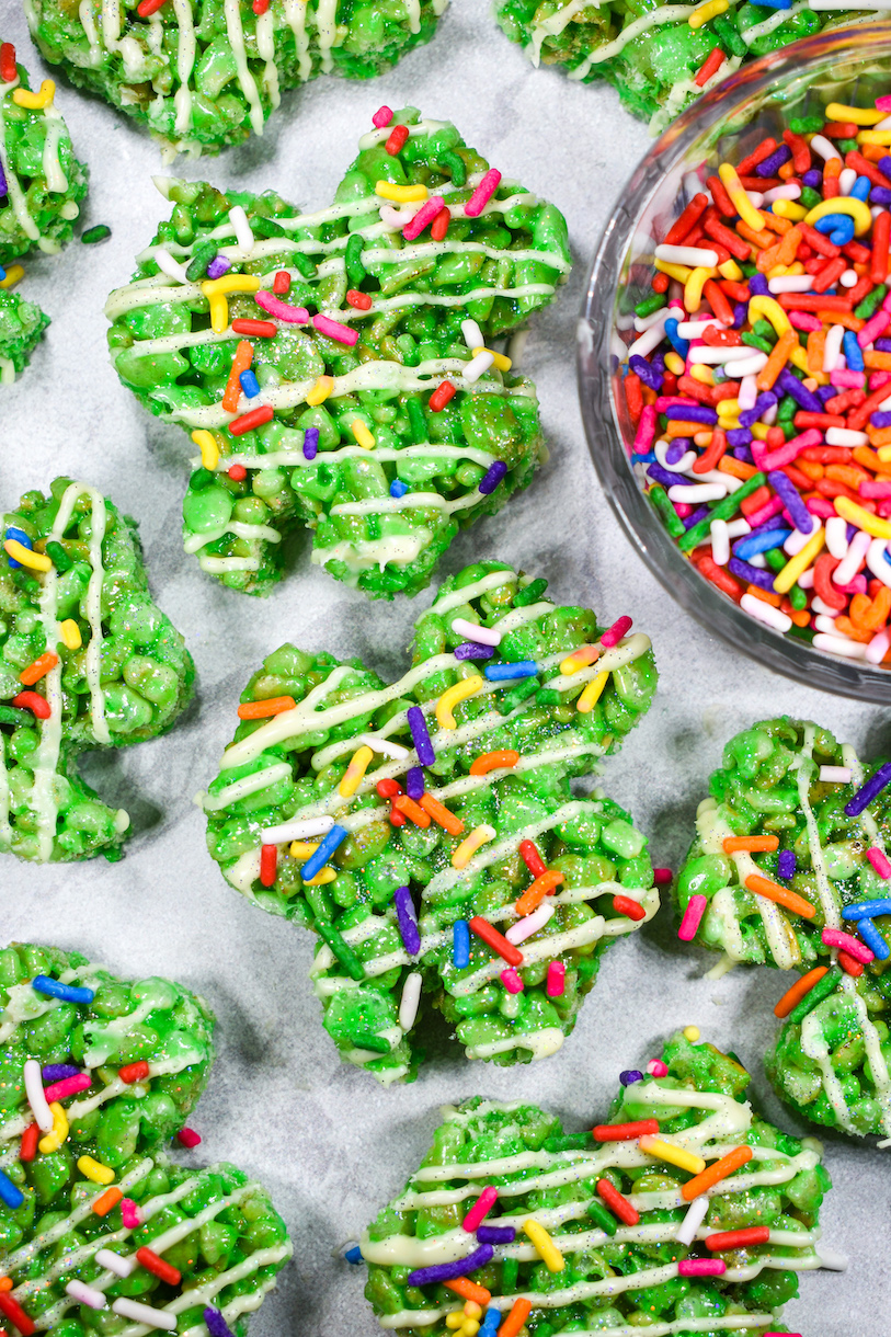 Shamrock Rice Krispie treats and a bowl of rainbow sprinkles on a white surface