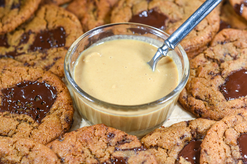 A dish of tahini and a spoon, surrounded by cookies