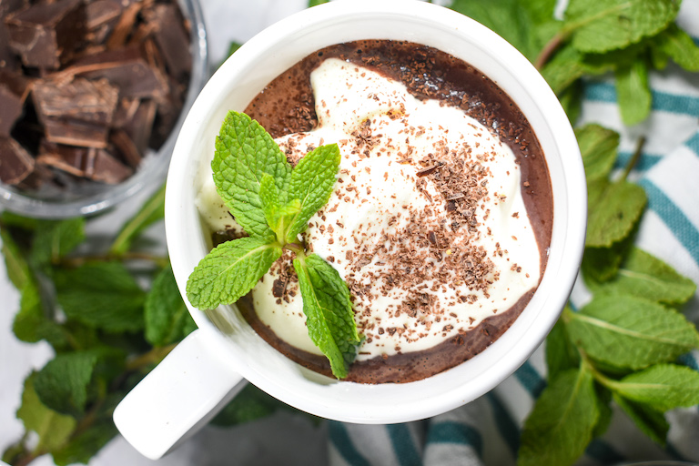Peppermint cocoa in a mug with whipped cream, shaved chocolate and fresh mint